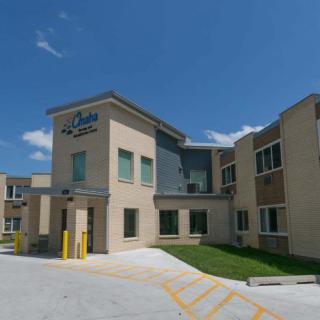 A hotel building with a modern design and parking area under a clear blue sky.