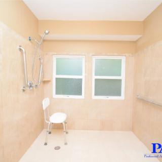 A spacious, accessible bathroom with handrails and a chair.