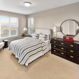 A cozy bedroom with a striped bedspread, a dresser with a mirror, and large windows.