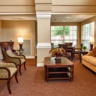 A cozy living room with elegant furniture, including chairs and a sofa, illuminated by lamps and natural light from the windows.