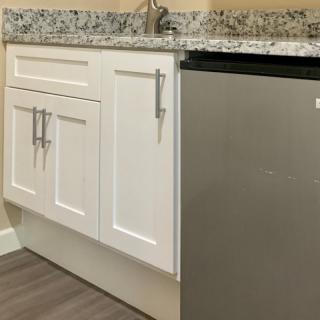 A modern kitchen area featuring white cabinets, a granite countertop, and a compact fridge.