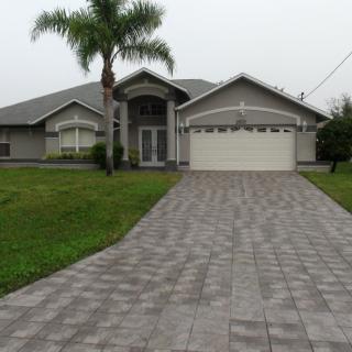 A suburban house with a large driveway and palm trees in the front yard.