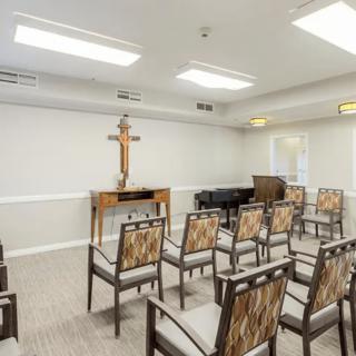 A small chapel with arranged chairs, a cross at the front, and a piano in the corner.