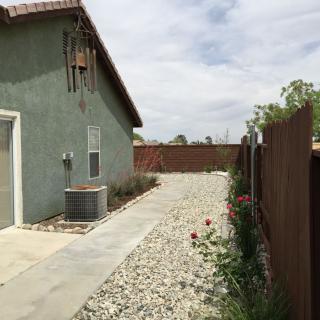 A side yard with gravel and plants alongside a house, with a wooden fence and an air conditioning unit.