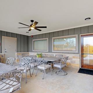 A stylish outdoor patio featuring a dining area with metal furniture, complemented by a ceiling fan and large windows for natural light.