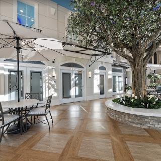 A modern indoor area with a tree, seating, and umbrellas, resembling a commercial or communal space.
