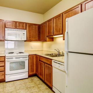 A modern kitchen featuring wooden cabinets, a refrigerator, oven, microwave, and a dishwasher.