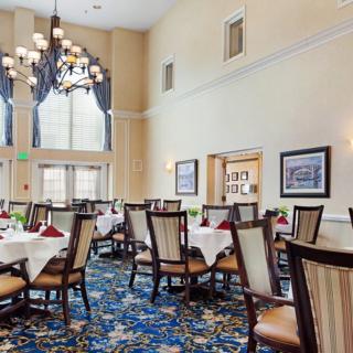 An elegant dining room with beautifully set tables, upholstered chairs, and a large chandelier.