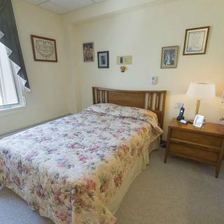 A cozy vintage-style bedroom with a floral bedspread, wooden headboard, and a nightstand with a lamp.