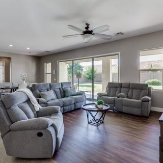 A spacious and modern living room with comfortable sofas, large windows, and a ceiling fan.