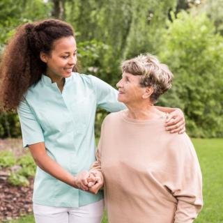 A caregiver and an elderly woman enjoying a walk in the garden, sharing a moment of companionship.