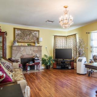 A cozy living room with hardwood floors, featuring a chandelier, sofa, fireplace, and television.