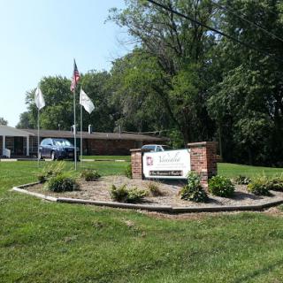 A welcoming entrance with signage, surrounded by greenery and flags.