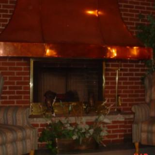 A cozy living room with a copper-hooded fireplace and brick wall.