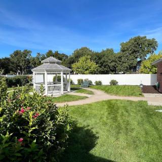 A serene garden featuring a gazebo surrounded by lush greenery and a clear blue sky.