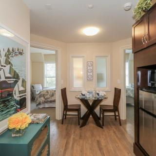 A cozy dining area with modern decor, featuring a table set for two and surrounded by vibrant artwork and wooden cabinetry.