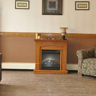 A cozy living room features a small wooden fireplace, surrounded by patterned sofas and decorated with framed artwork.