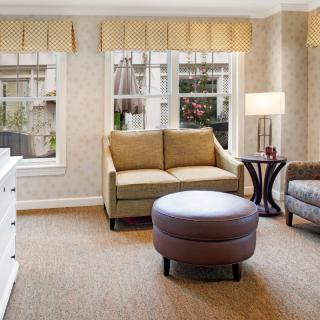 A cozy living room with a sofa, ottoman, and large windows.