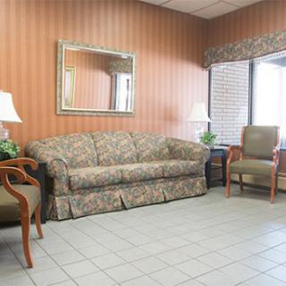 A cozy waiting area featuring a floral sofa, armchair, and indoor plants against a patterned wall.