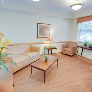 A cozy living room with a sofa, armchair, and coffee table, adorned with artwork and indoor plants.