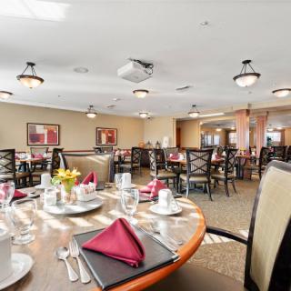 A well-decorated dining room with neatly arranged tables and chairs, set with plates, glasses, and napkins.