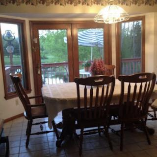 A cozy dining room featuring a wooden table and chairs, illuminated by natural light through large windows.