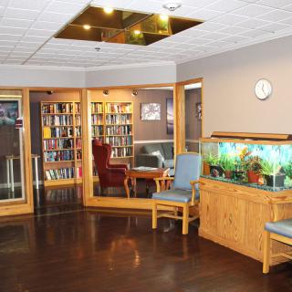A cozy library corner with bookshelves, armchairs, and an aquarium, creating a welcoming waiting area.