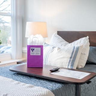 A well-lit hospital room with a comfortable bed and a tray table equipped with essentials.