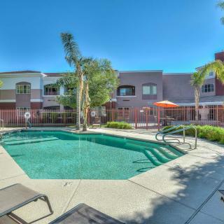 A serene outdoor pool area at an apartment complex, surrounded by palm trees and patio furniture under a clear blue sky.