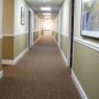 A long, carpeted hallway with closed doors and framed pictures on the walls.