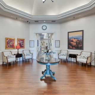 A modern waiting room featuring elegant chairs, vibrant artwork, a central table with decor, and a wall clock.