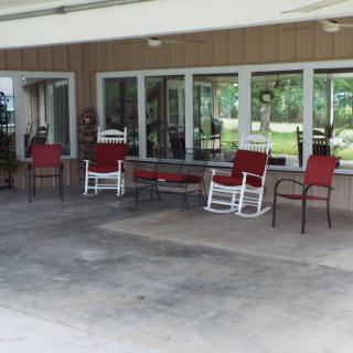 A cozy outdoor patio with red cushioned chairs and rocking chairs under a covered area.