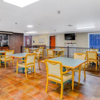 A bright indoor dining area with several tables and chairs, featuring a tiled floor and a television.