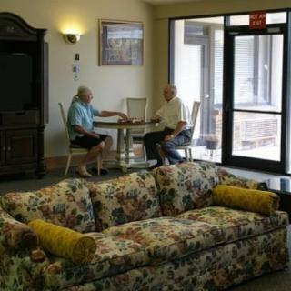 Two people sitting at a table in a living room with floral-patterned sofa.