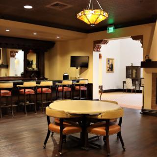 A cozy lounge area featuring a table with chairs and a bar in the background.