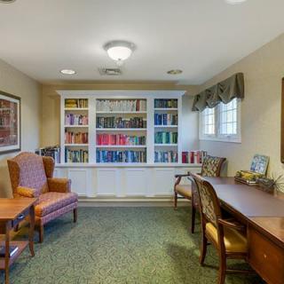 A cozy library room with books neatly arranged on shelves, featuring comfortable chairs and a long table for reading or study.