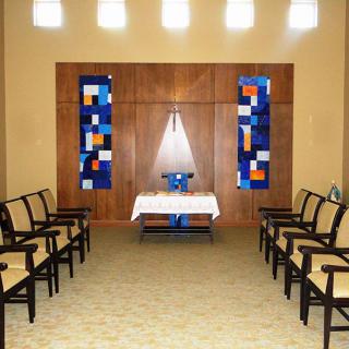A serene chapel interior with aligned seating, an altar at the front, and decorative lighting.