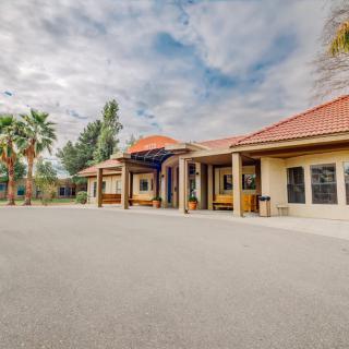 A wide view of a building entrance surrounded by palm trees under a cloudy sky.