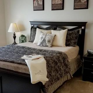 A neatly arranged bedroom with a dark wooden bedframe, patterned bedding, and decorative pillows. A lamp sits on the nightstand beside the bed.