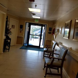 A well-lit hallway featuring a waiting area with chairs and a clear entrance door.