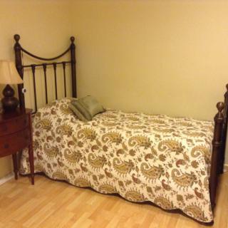 A cozy bedroom setup featuring a single bed with a patterned comforter, a decorative pillow, and a small wooden nightstand with a lamp.