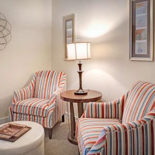 A cozy corner featuring striped chairs, a side table with a lamp, and tasteful wall decor.