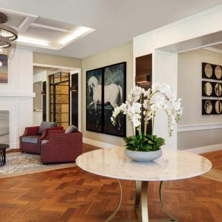A modern living room with elegant decor, featuring a round table with orchids, artwork on the walls, and comfortable seating.