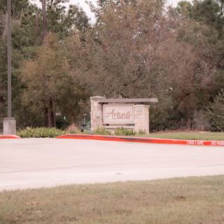 Entrance sign surrounded by trees and a road.
