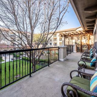 A spacious balcony with comfortable chairs overlooks a peaceful courtyard in an apartment complex.