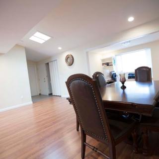 A spacious dining room with a large wooden table and chairs, featuring bright lighting and a wooden floor.