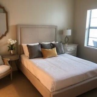 A neatly arranged bedroom with a bed, pillows, and natural lighting.