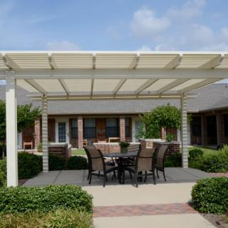 A patio with a pergola providing shade over an outdoor dining set, surrounded by well-maintained garden landscaping.