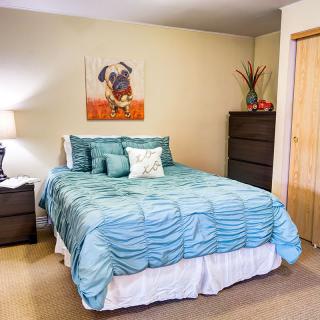 A cozy bedroom featuring a bed with a blue bedspread, a nightstand with a lamp, and wall art.