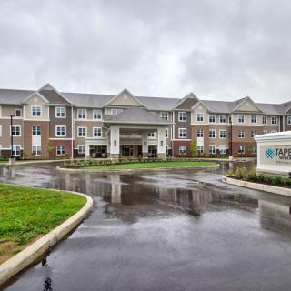A modern senior living facility on a rainy day with well-maintained landscaping and clear signage.